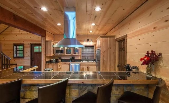 kitchen featuring appliances with stainless steel finishes, wood ceiling, island range hood, wooden walls, and tile countertops