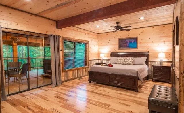 bedroom with access to exterior, ceiling fan, beam ceiling, light hardwood / wood-style floors, and wood walls