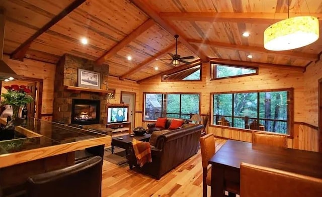 living room with wooden ceiling, a stone fireplace, wooden walls, vaulted ceiling with beams, and light hardwood / wood-style floors