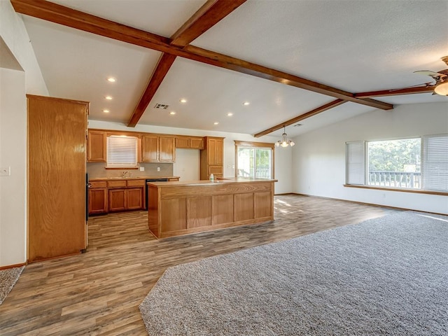 kitchen with lofted ceiling with beams, a kitchen island with sink, a healthy amount of sunlight, and light wood-type flooring