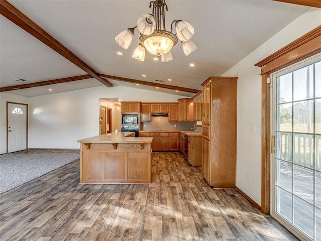 kitchen featuring stainless steel microwave, lofted ceiling with beams, a notable chandelier, a center island with sink, and light wood-type flooring