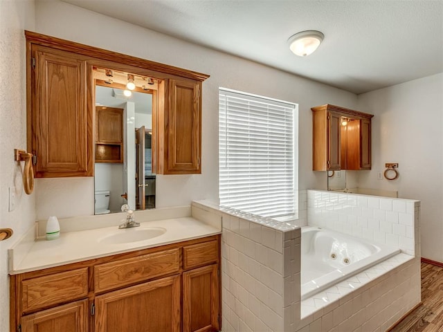 bathroom featuring tiled bath, vanity, hardwood / wood-style flooring, and toilet