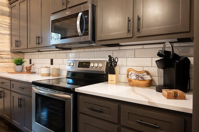 kitchen featuring backsplash, gray cabinetry, light stone countertops, and appliances with stainless steel finishes