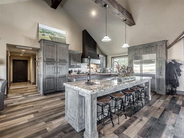 kitchen with premium range hood, hanging light fixtures, dark hardwood / wood-style floors, a kitchen island, and stainless steel built in refrigerator