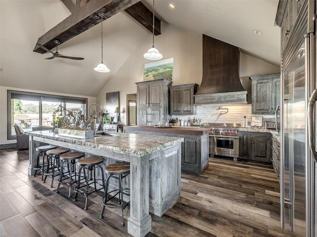 kitchen featuring dark wood-type flooring, premium appliances, high vaulted ceiling, an island with sink, and custom range hood