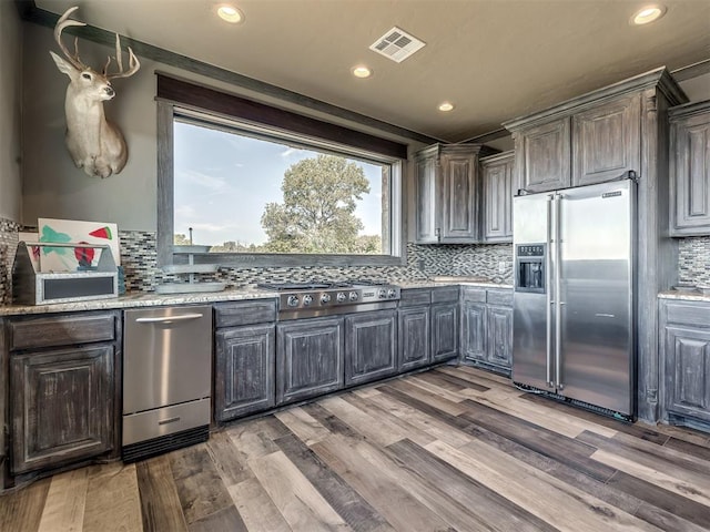 kitchen featuring dark brown cabinetry, wood-type flooring, stainless steel appliances, and tasteful backsplash