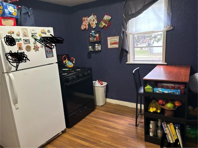 kitchen featuring black stove, white fridge, and hardwood / wood-style flooring