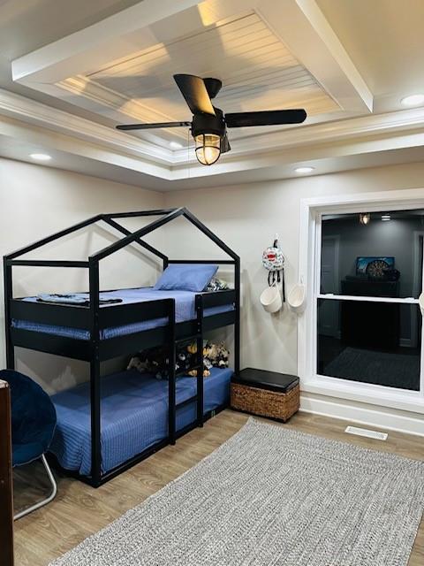 bedroom featuring hardwood / wood-style flooring, ceiling fan, ornamental molding, and a tray ceiling