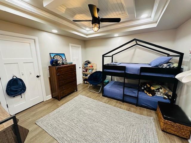 bedroom with a tray ceiling, light hardwood / wood-style flooring, ceiling fan, and crown molding