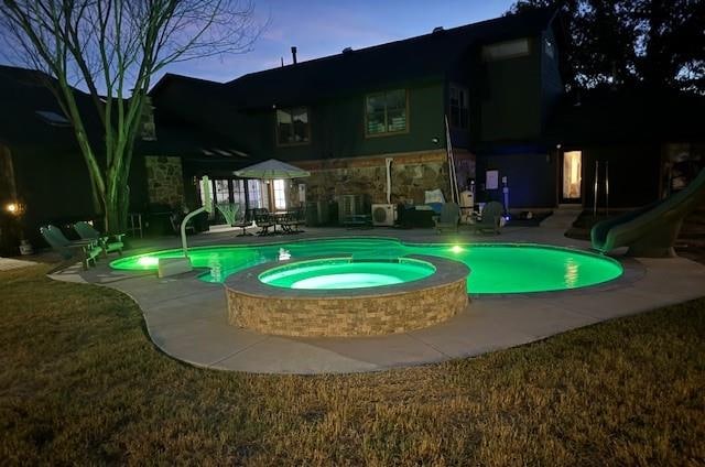 pool at dusk with an in ground hot tub, a water slide, and a patio