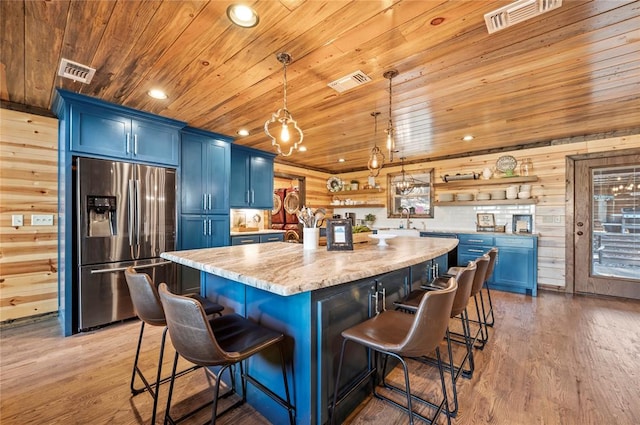 kitchen featuring visible vents, stainless steel refrigerator with ice dispenser, blue cabinetry, and open shelves