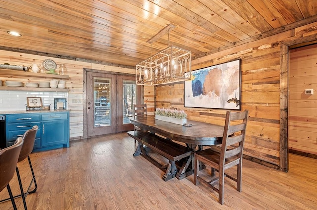 dining area featuring an inviting chandelier, light wood-type flooring, wood ceiling, and wooden walls