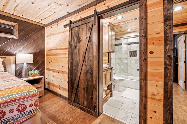 unfurnished bedroom with ensuite bathroom, a barn door, wooden ceiling, wooden walls, and marble finish floor