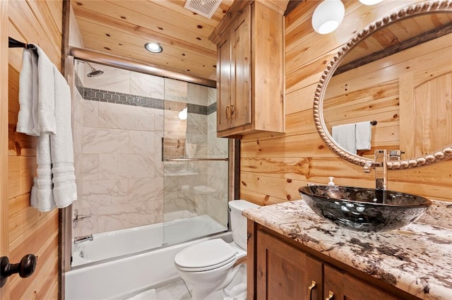 full bath with bath / shower combo with glass door, visible vents, toilet, wood walls, and vanity