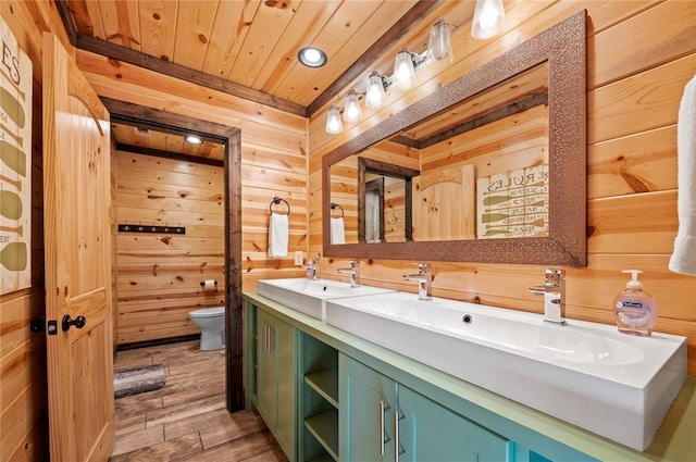 full bath with wooden walls, toilet, wood ceiling, wood finished floors, and a sink