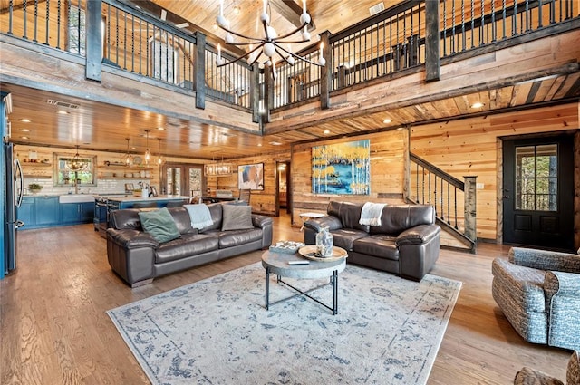 living room featuring wooden ceiling, a high ceiling, light hardwood / wood-style flooring, wood walls, and a chandelier