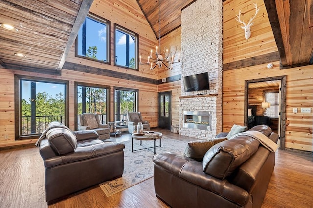 living area featuring a chandelier, a stone fireplace, wooden ceiling, wood walls, and wood finished floors