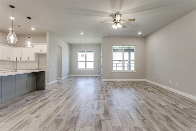 unfurnished living room featuring ceiling fan with notable chandelier, light wood-type flooring, and sink