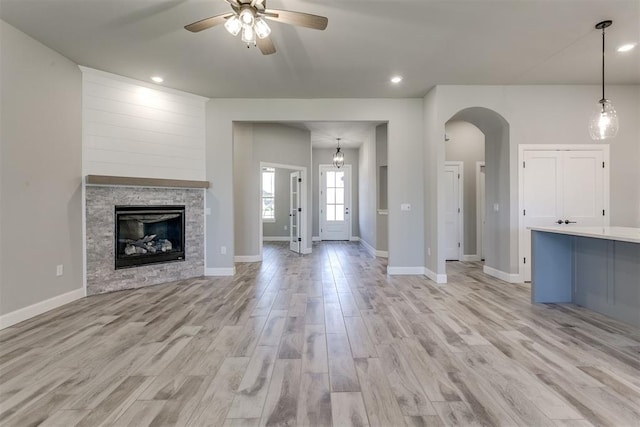 unfurnished living room with ceiling fan, light hardwood / wood-style floors, and a stone fireplace