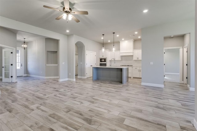 kitchen with white cabinetry, hanging light fixtures, a kitchen island with sink, appliances with stainless steel finishes, and light wood-type flooring