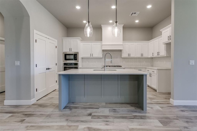 kitchen featuring appliances with stainless steel finishes, a center island with sink, white cabinetry, and decorative light fixtures