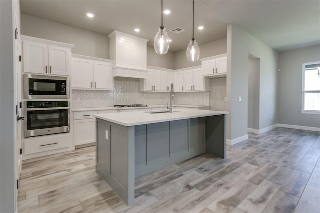 kitchen with white cabinetry, sink, stainless steel appliances, an island with sink, and decorative light fixtures