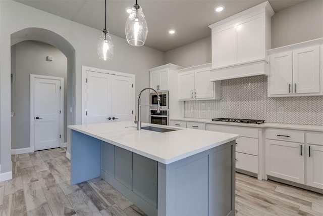 kitchen featuring white cabinets, decorative light fixtures, light hardwood / wood-style floors, and an island with sink