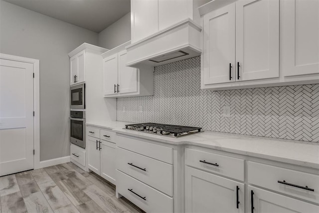 kitchen featuring decorative backsplash, light wood-type flooring, appliances with stainless steel finishes, light stone counters, and white cabinetry