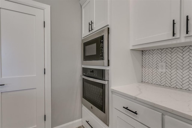 kitchen with light stone countertops, tasteful backsplash, black microwave, white cabinets, and oven