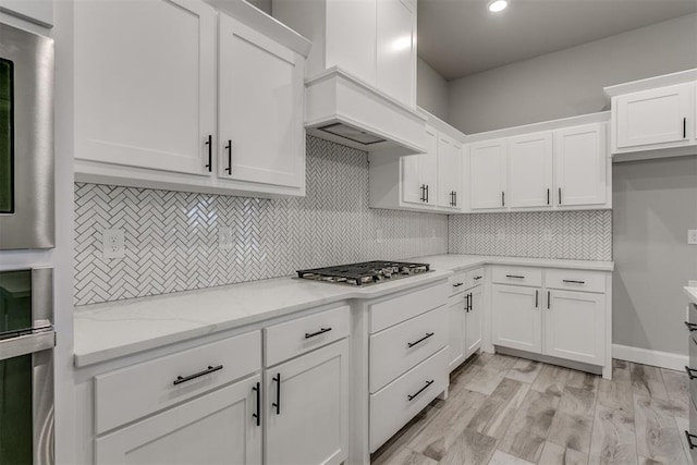 kitchen with backsplash, light stone counters, white cabinetry, and light wood-type flooring