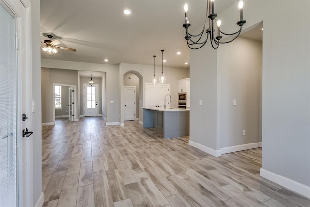 kitchen with sink, hanging light fixtures, a kitchen island with sink, appliances with stainless steel finishes, and light wood-type flooring