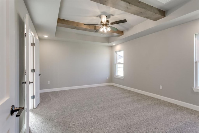 empty room featuring a tray ceiling, ceiling fan, beamed ceiling, and carpet