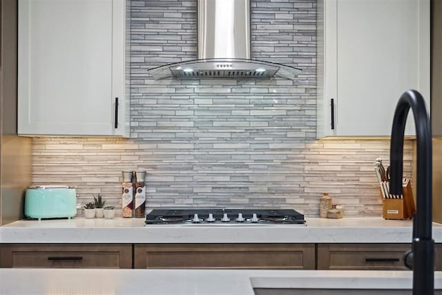 kitchen featuring backsplash, light stone counters, white cabinets, and wall chimney range hood