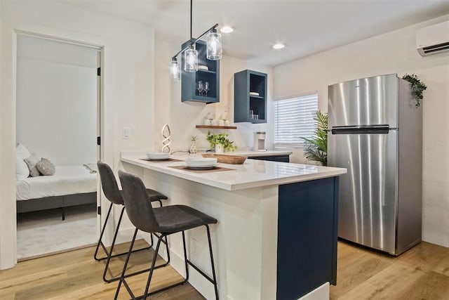 kitchen with light hardwood / wood-style flooring, stainless steel fridge, blue cabinetry, kitchen peninsula, and a breakfast bar area