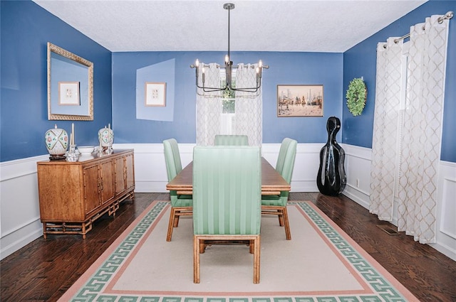 dining space featuring a textured ceiling, dark wood-style flooring, wainscoting, and a notable chandelier