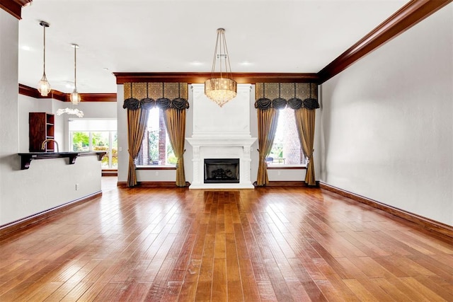 unfurnished living room with wood-type flooring, ornamental molding, a wealth of natural light, and a chandelier