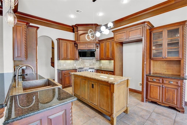 kitchen with pendant lighting, backsplash, dark stone counters, sink, and a kitchen island