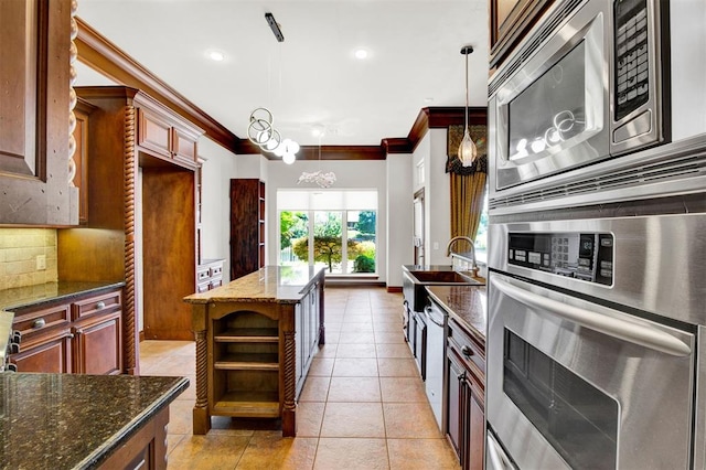 kitchen featuring appliances with stainless steel finishes, backsplash, crown molding, decorative light fixtures, and dark stone countertops