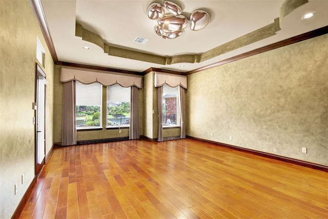 unfurnished room featuring a raised ceiling, ornamental molding, and hardwood / wood-style flooring