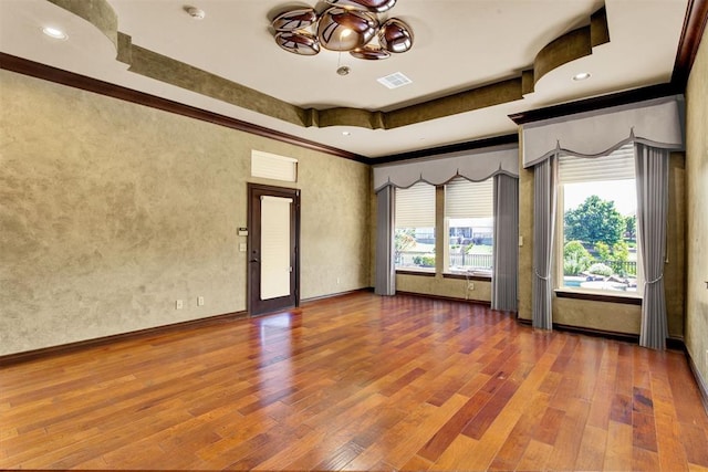 spare room with a raised ceiling, wood-type flooring, and ornamental molding