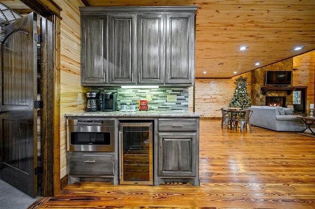 bar with wood walls, light stone counters, light wood-type flooring, and wine cooler