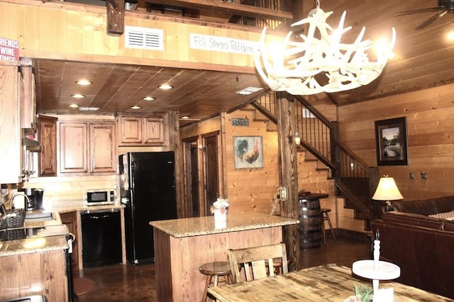 kitchen featuring a center island, wood walls, black appliances, dark hardwood / wood-style floors, and light stone countertops