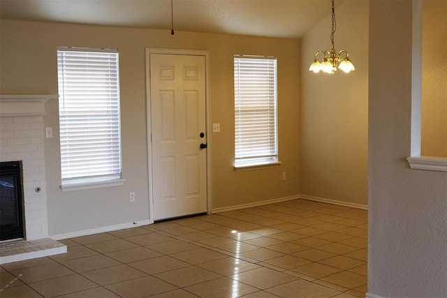 entrance foyer featuring a healthy amount of sunlight, light tile patterned floors, a chandelier, and a brick fireplace