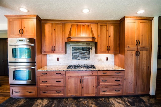 kitchen with light stone countertops, stainless steel appliances, tasteful backsplash, and custom exhaust hood