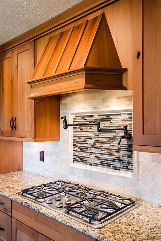 kitchen featuring premium range hood, decorative backsplash, light stone countertops, and stainless steel gas cooktop