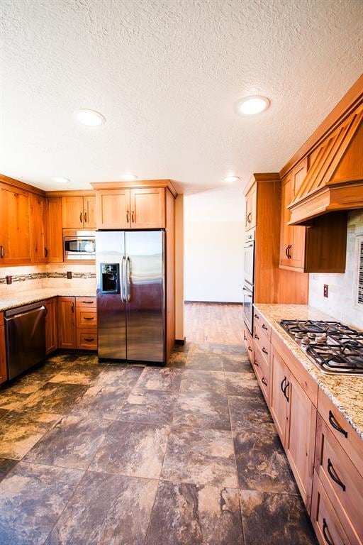 kitchen featuring light stone countertops, stainless steel appliances, and a textured ceiling