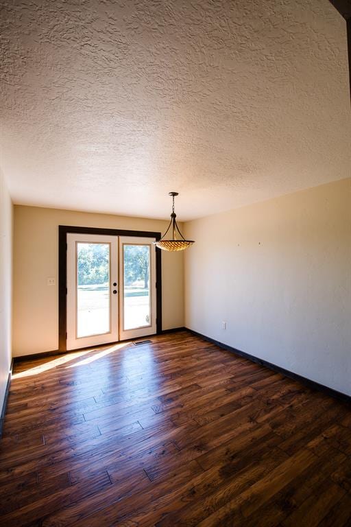 empty room featuring french doors, dark wood-type flooring, and a textured ceiling