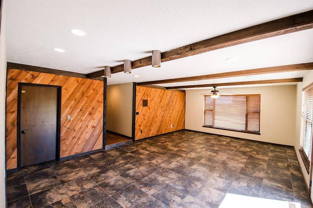 empty room with beamed ceiling, ceiling fan, and wood walls