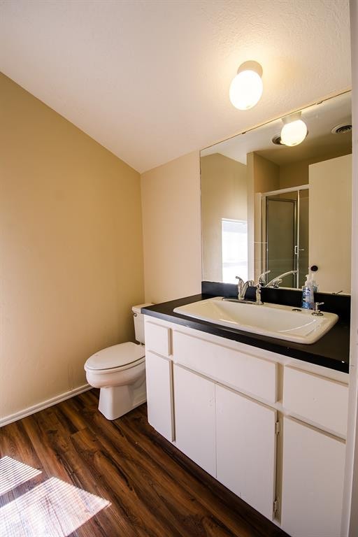 bathroom featuring wood-type flooring, vanity, toilet, and a shower with shower door