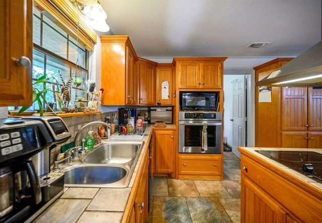 kitchen featuring island range hood, black microwave, sink, oven, and tile counters